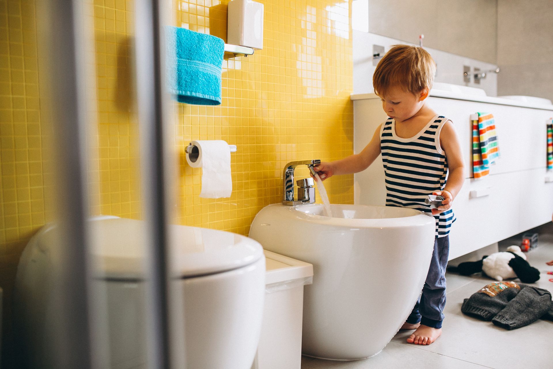 A little boy is standing next to a bidet in a bathroom.