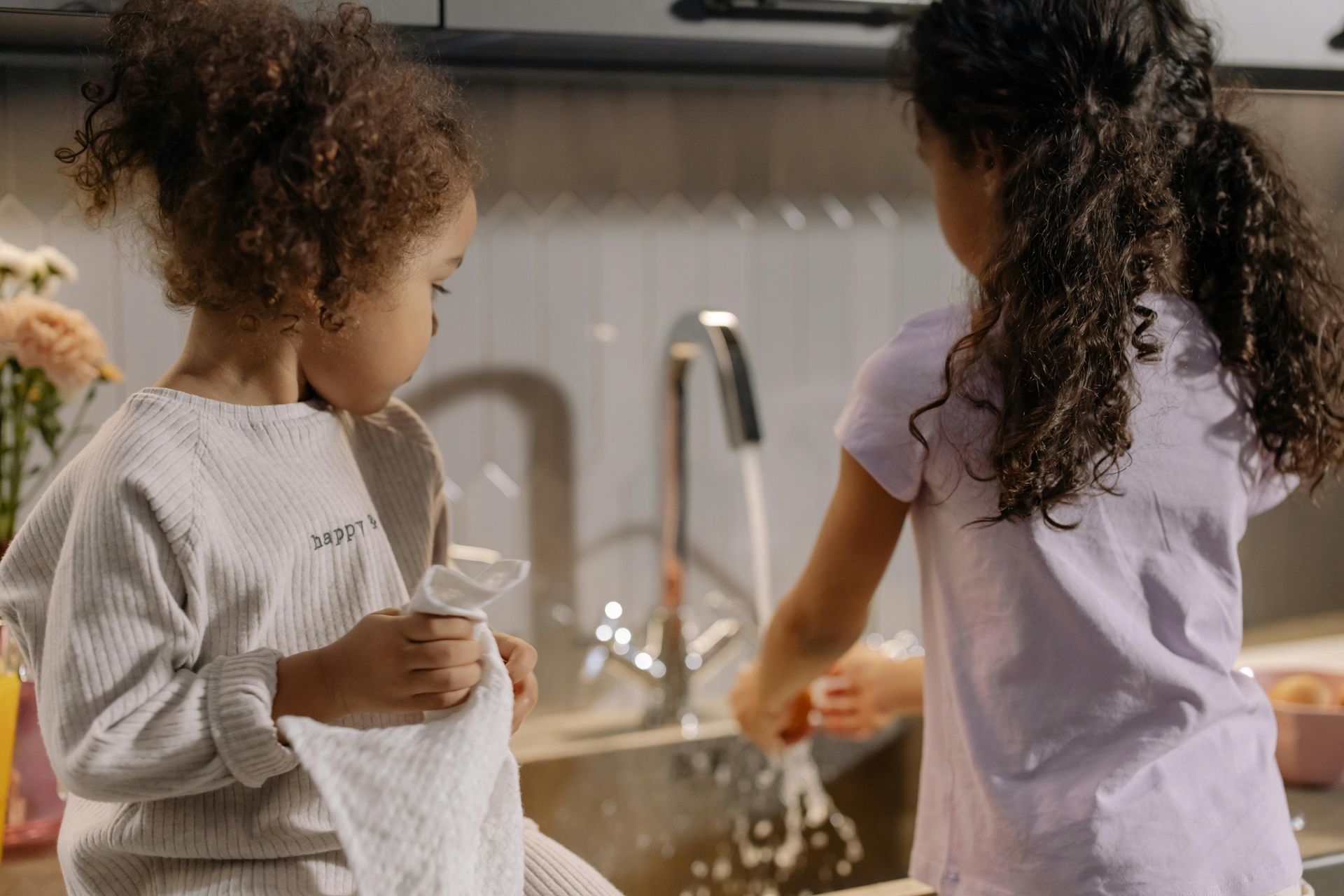 Two little girls are washing dishes in a kitchen sink.