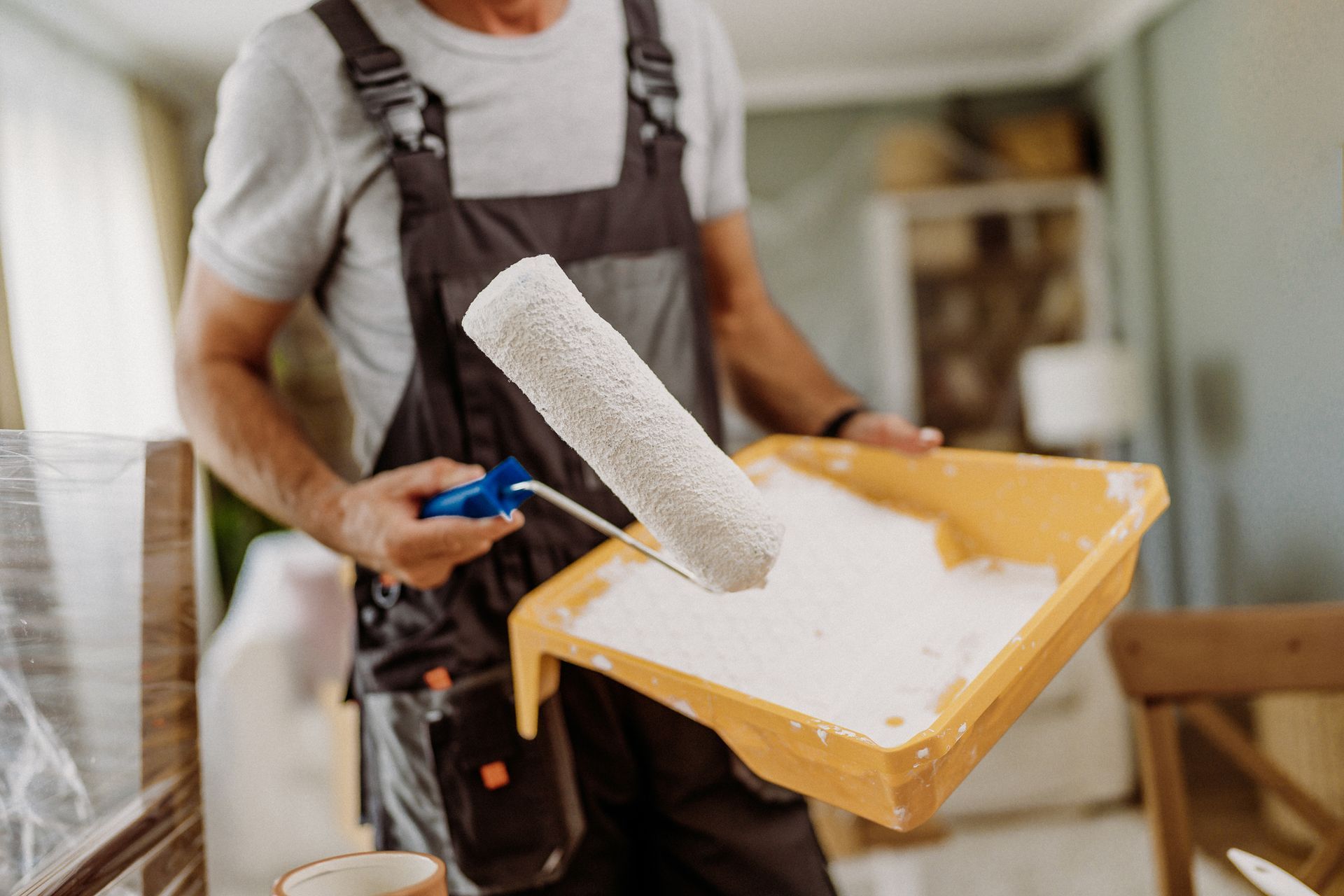 A man is holding a paint roller and a tray of paint.