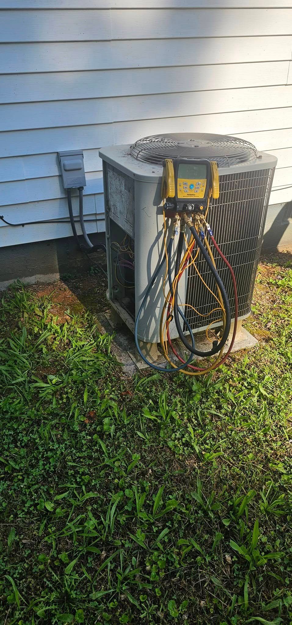 An outdoor air conditioning unit sits on a patch of green grass next to a light blue house.