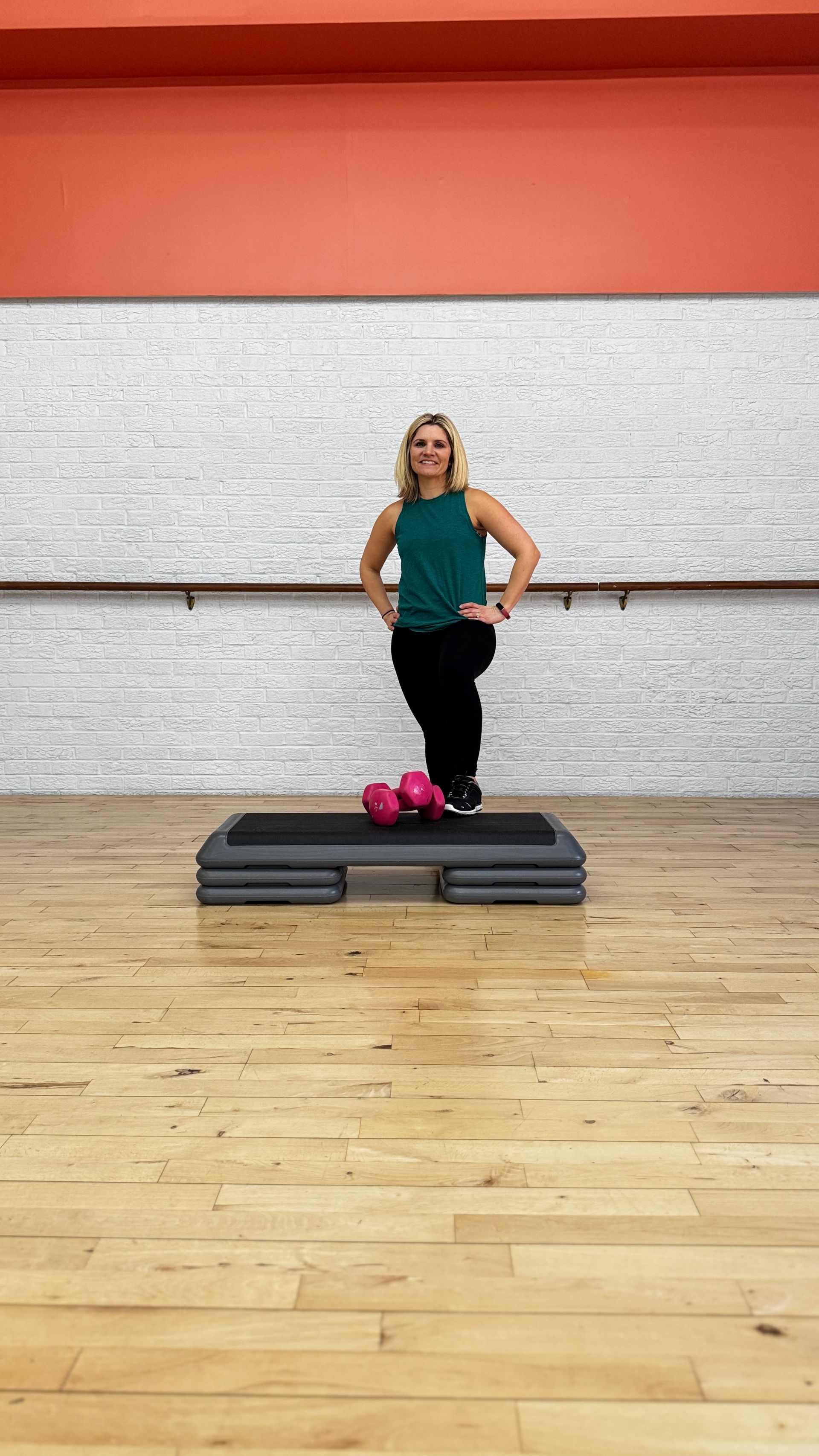 A woman is standing in front of a rack of dumbbells in a gym.