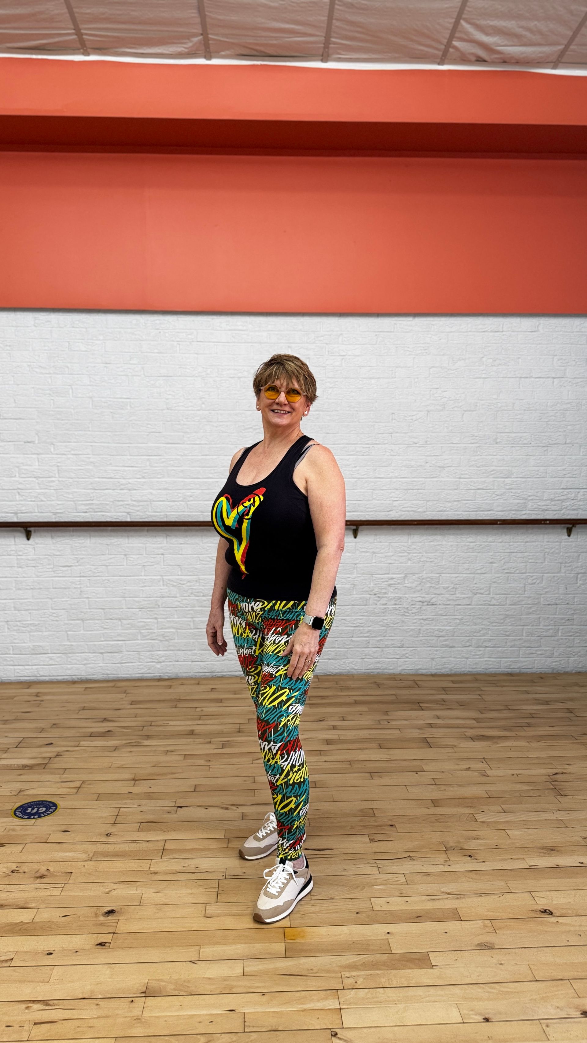 A woman is standing on a wooden floor in a dance studio.