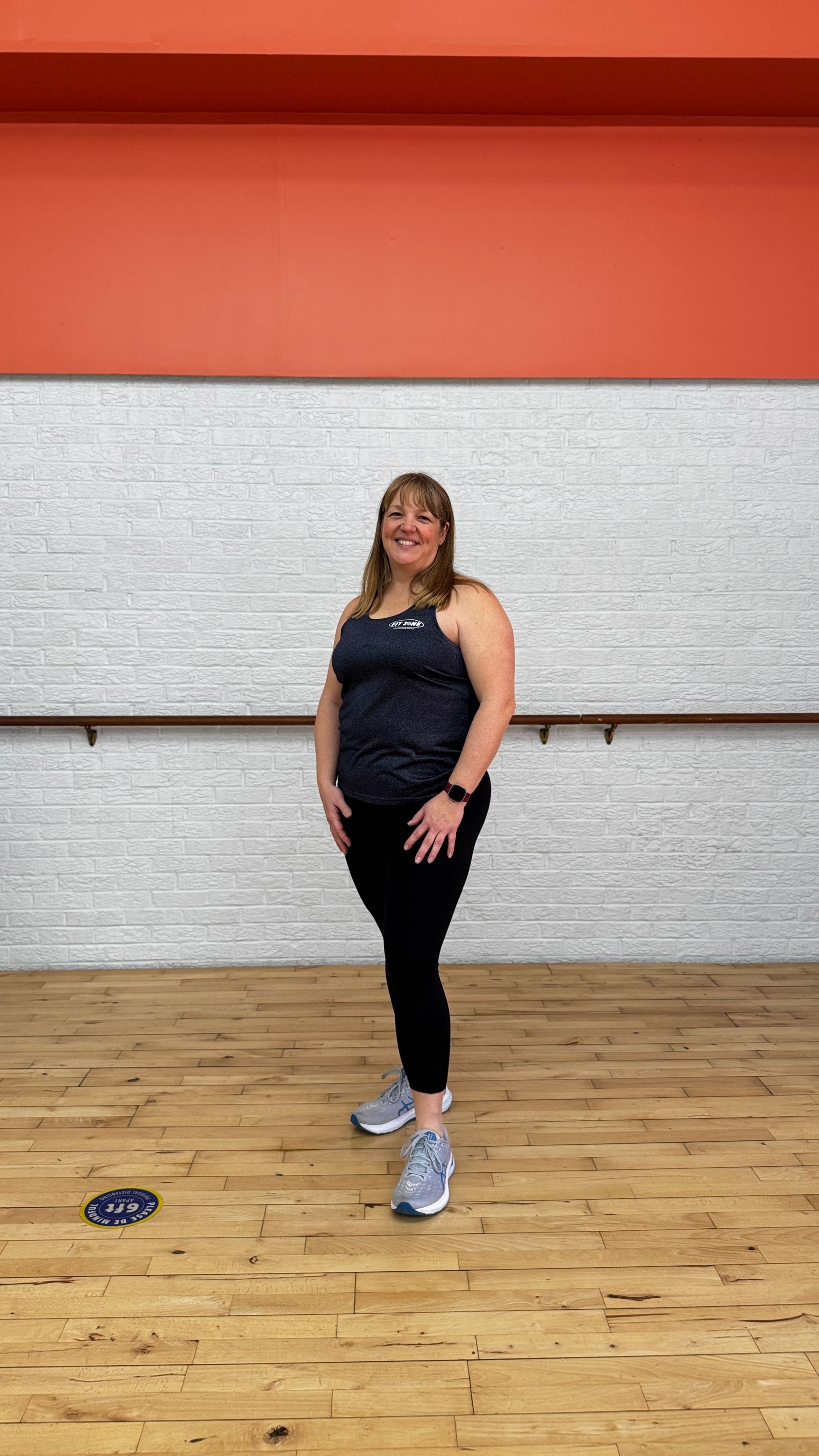 A woman is standing on a wooden floor in a dance studio.