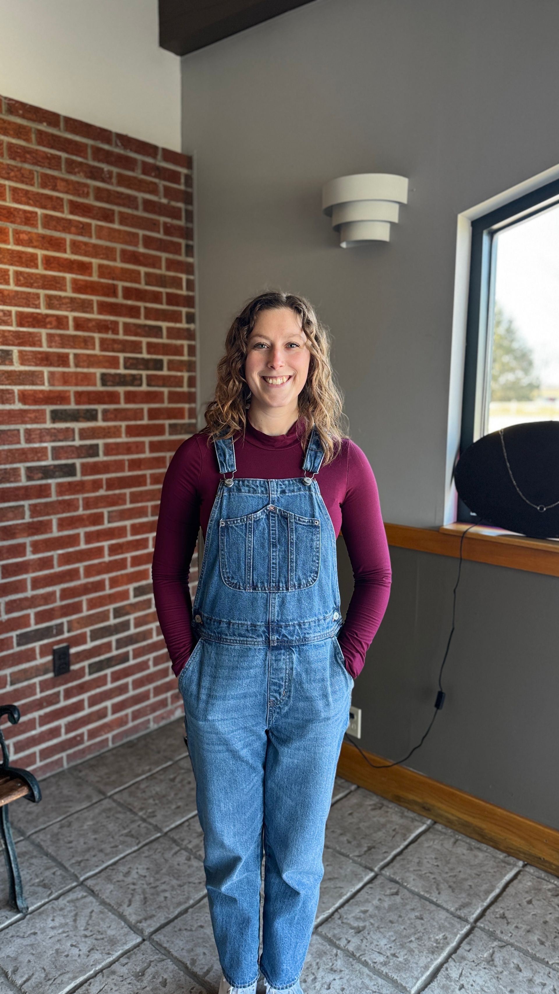 A woman in a white sweater is smiling in front of a brick wall.