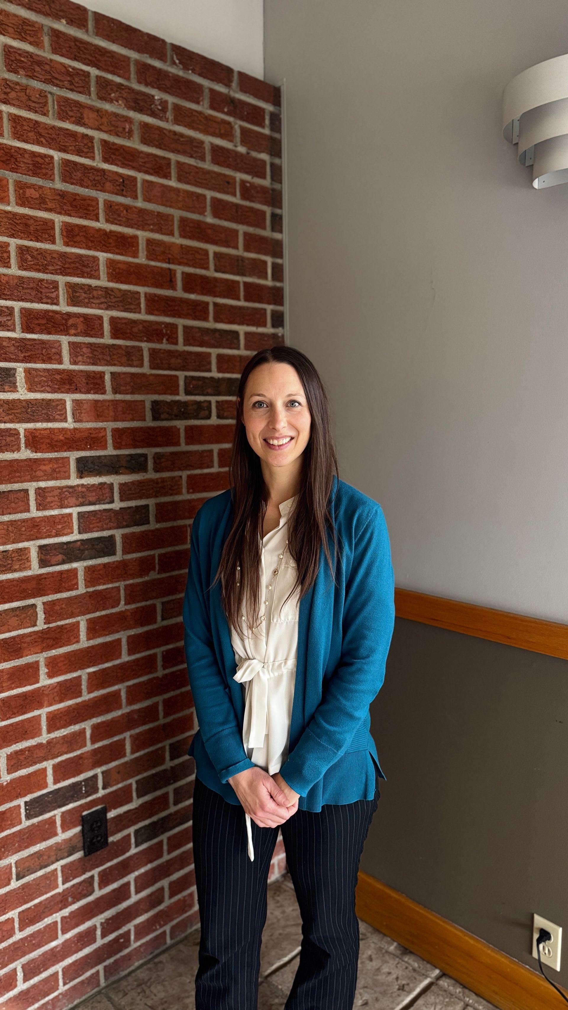A woman is smiling in front of a brick wall