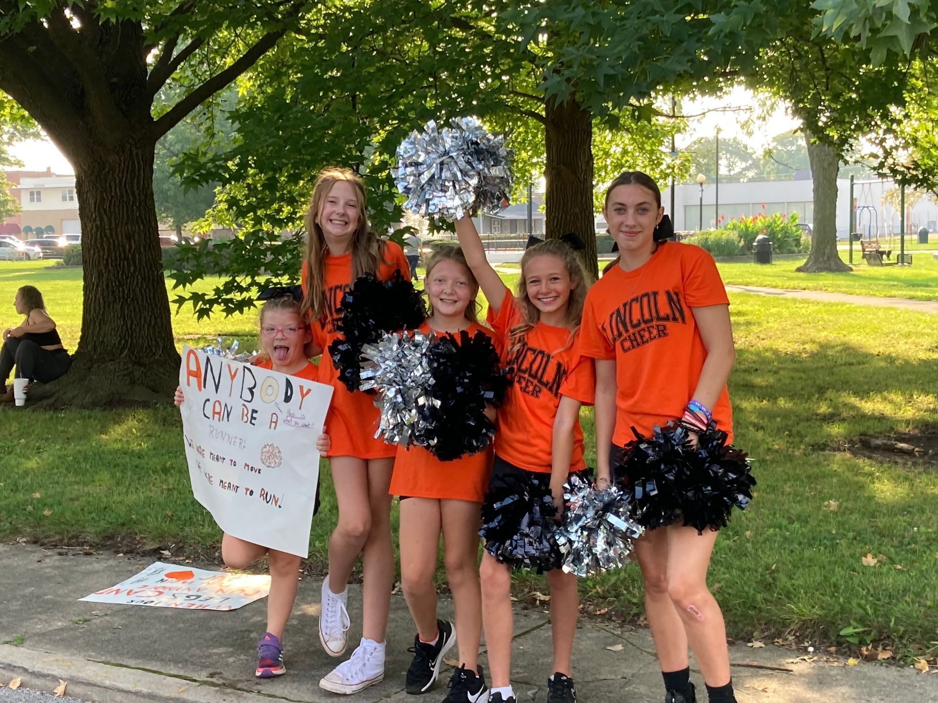 A group of young girls are holding pom poms and a sign.