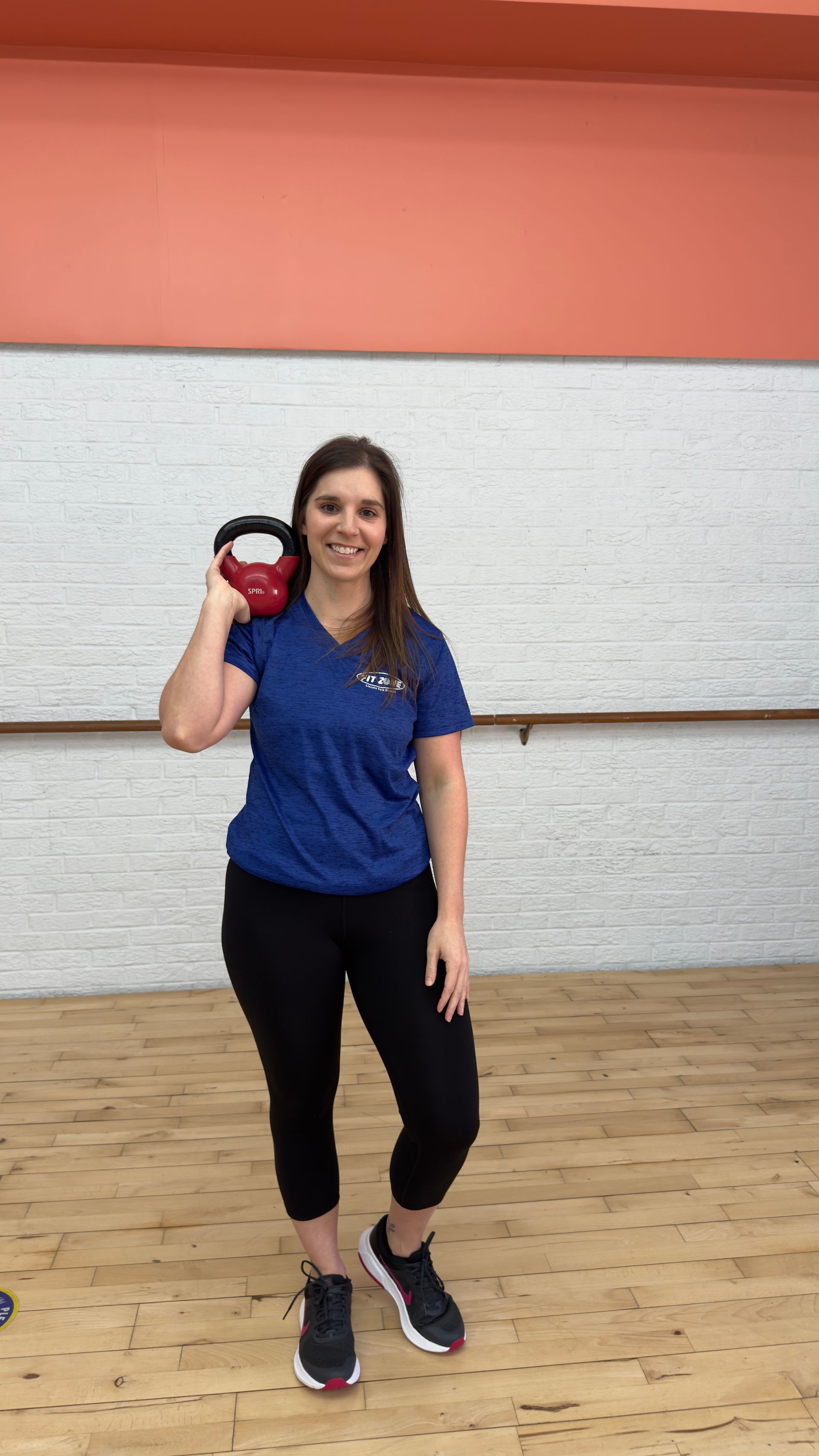 A woman is holding a kettlebell in her hand in a gym.