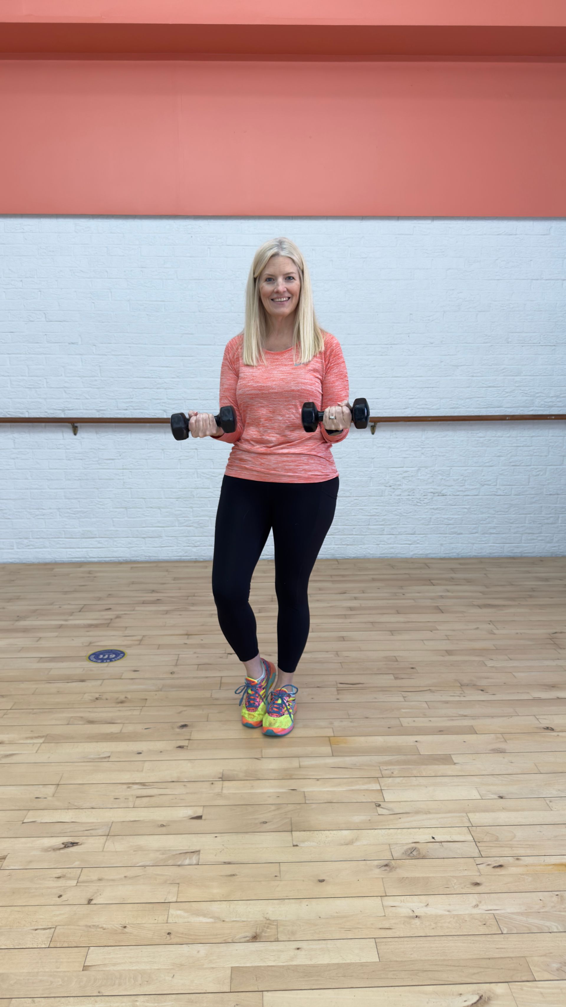 A woman is holding a pair of dumbbells in a dance studio.