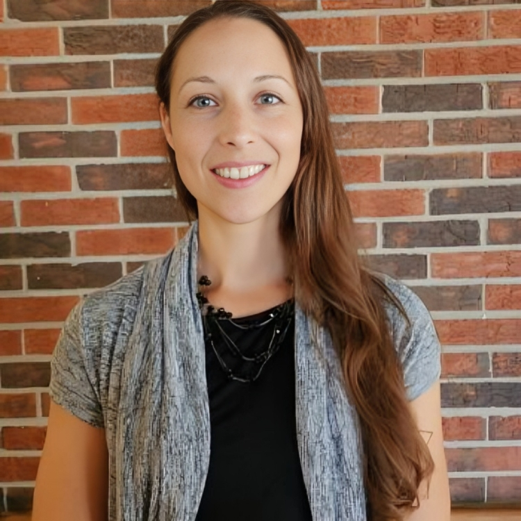 A woman is smiling in front of a brick wall