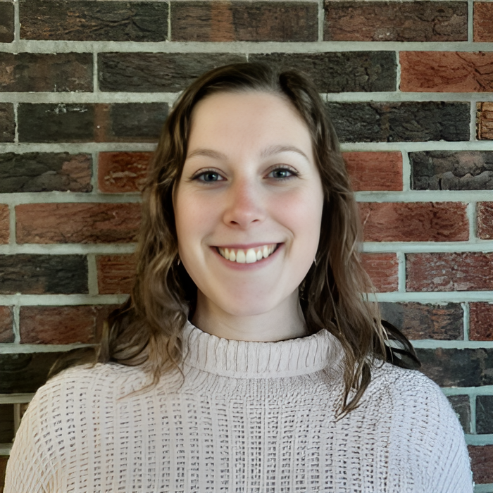 A woman in a white sweater is smiling in front of a brick wall.
