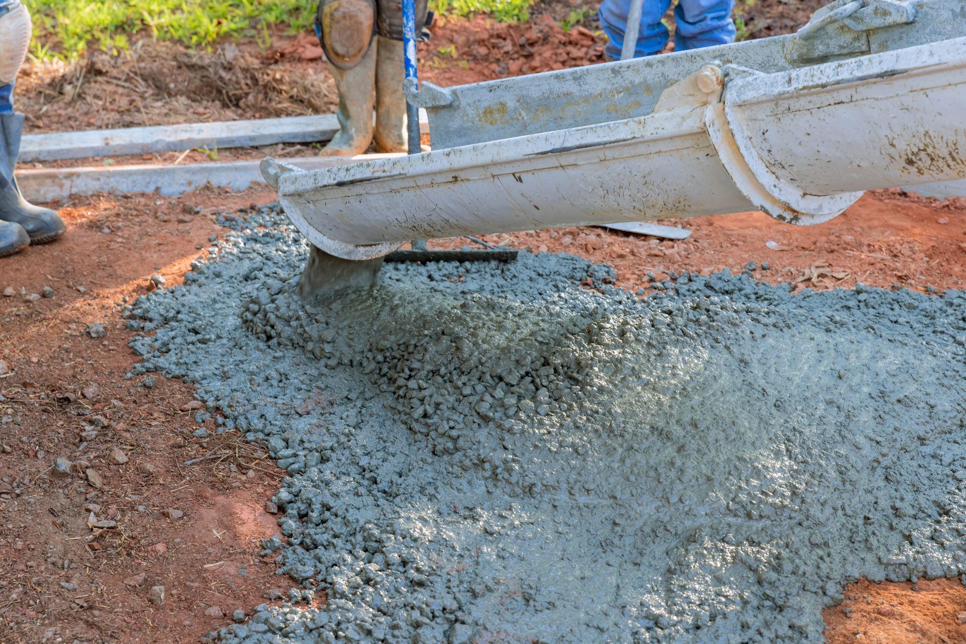 A concrete construction crew pouring wet concrete to pave a driveway on site.