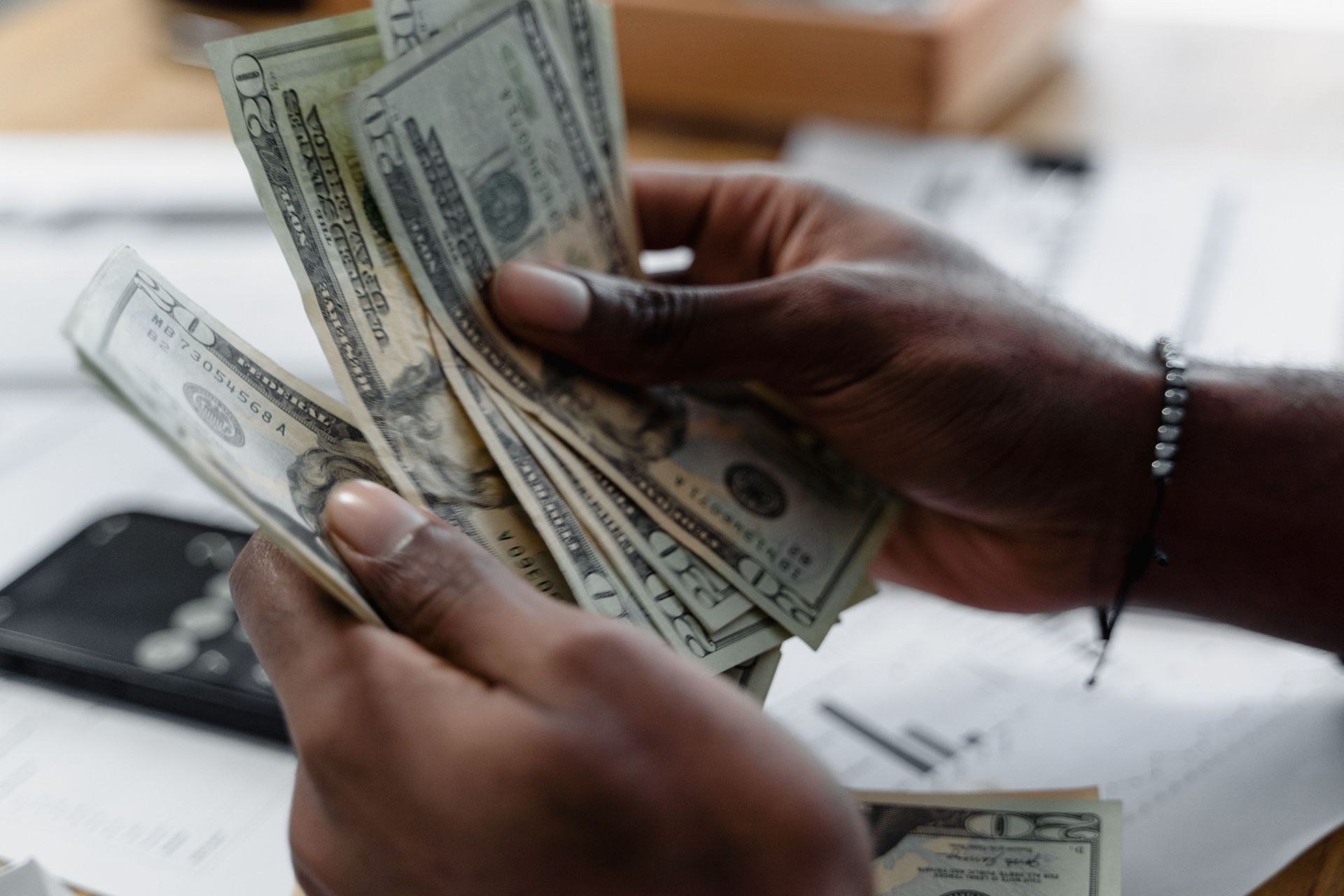 Hands counting U.S. dollar bills over a table with a calculator in the background