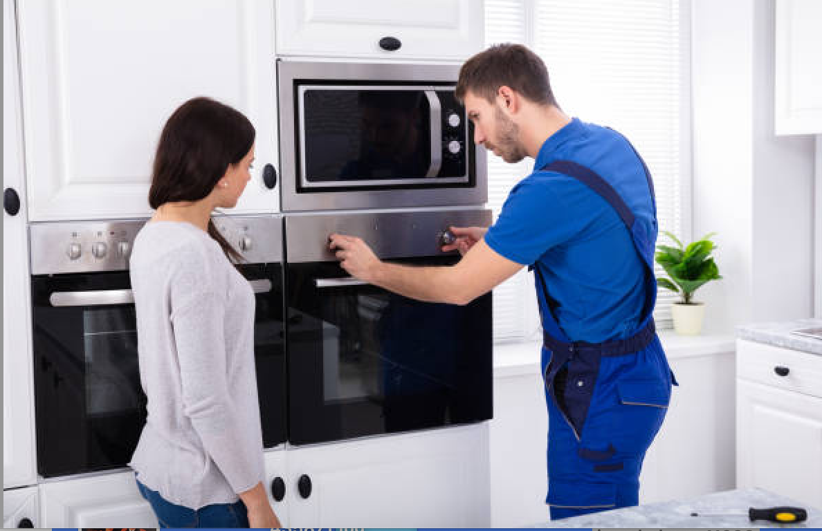 Technician in blue uniform fixing a built-in oven, woman watches in kitchen.