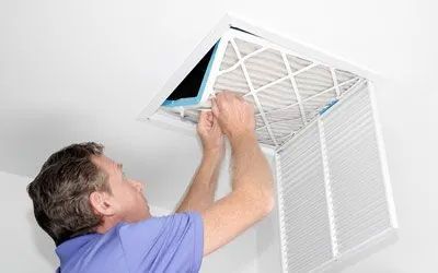 Man replacing an air filter in a ceiling vent.