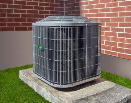 Air conditioning unit on a concrete pad next to a brick wall and artificial green grass.