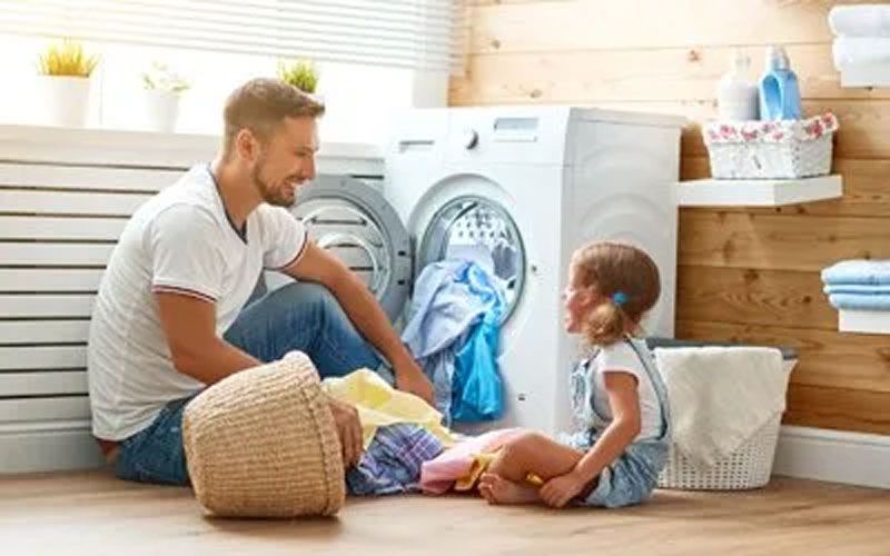 Man and child sorting laundry together near a washing machine.