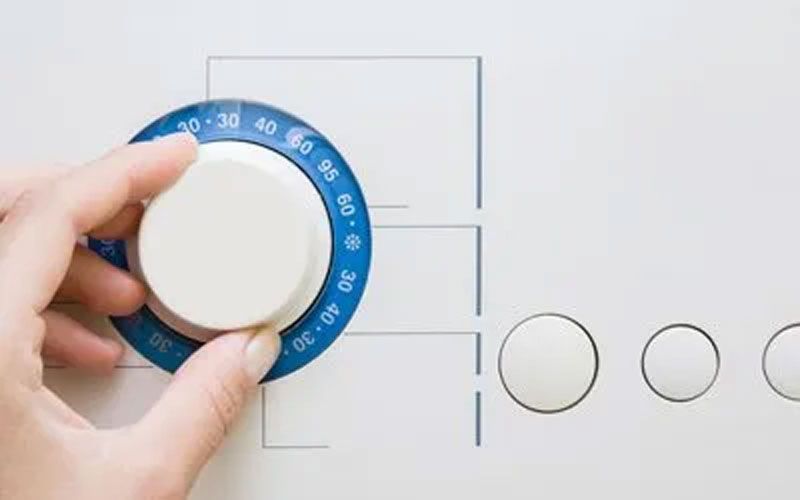 Hand turning a white knob with blue temperature markings on a white appliance.