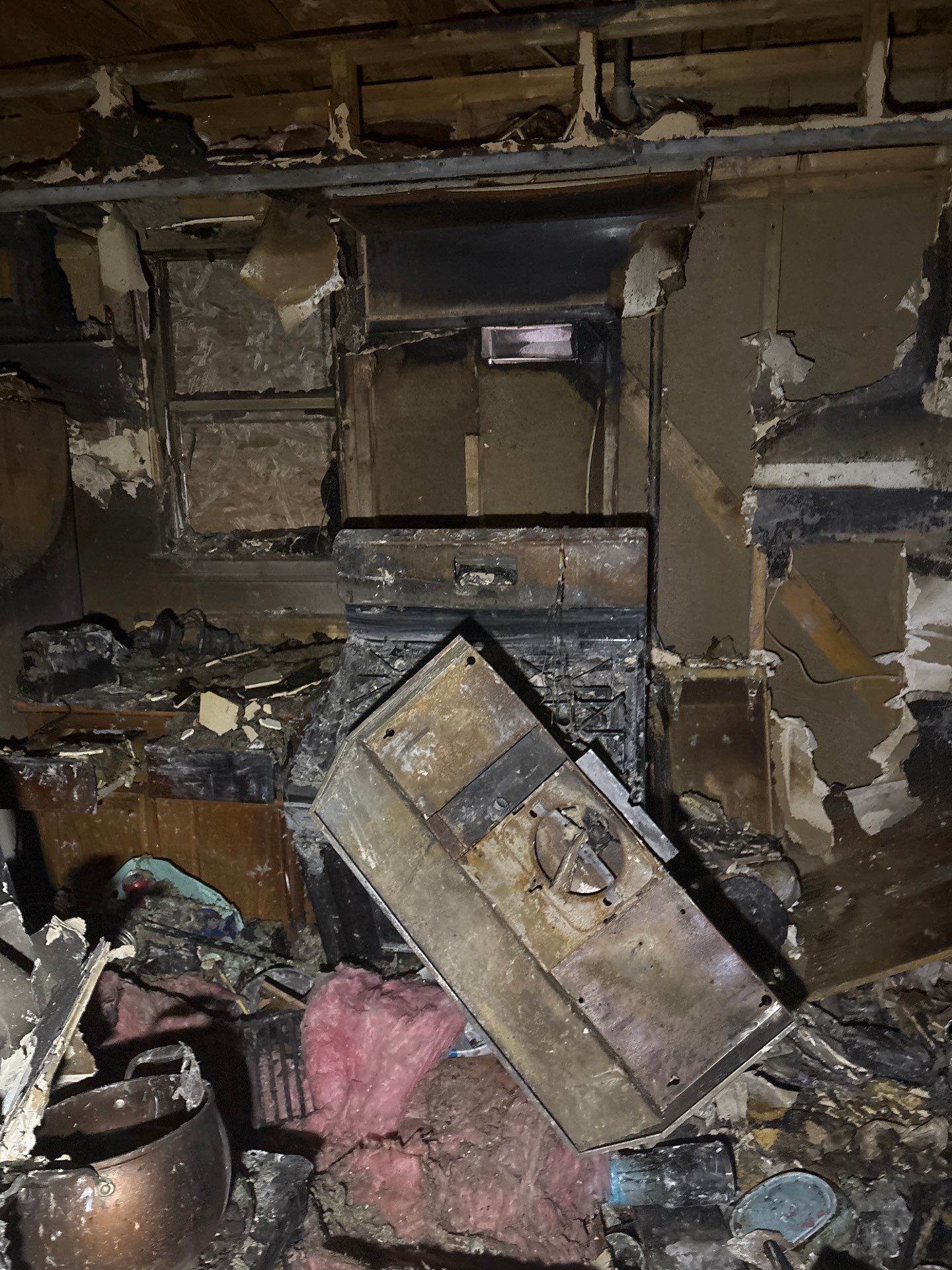Empty, dilapidated room with green and white walls, two doorways, and sunlight on the wood floor.