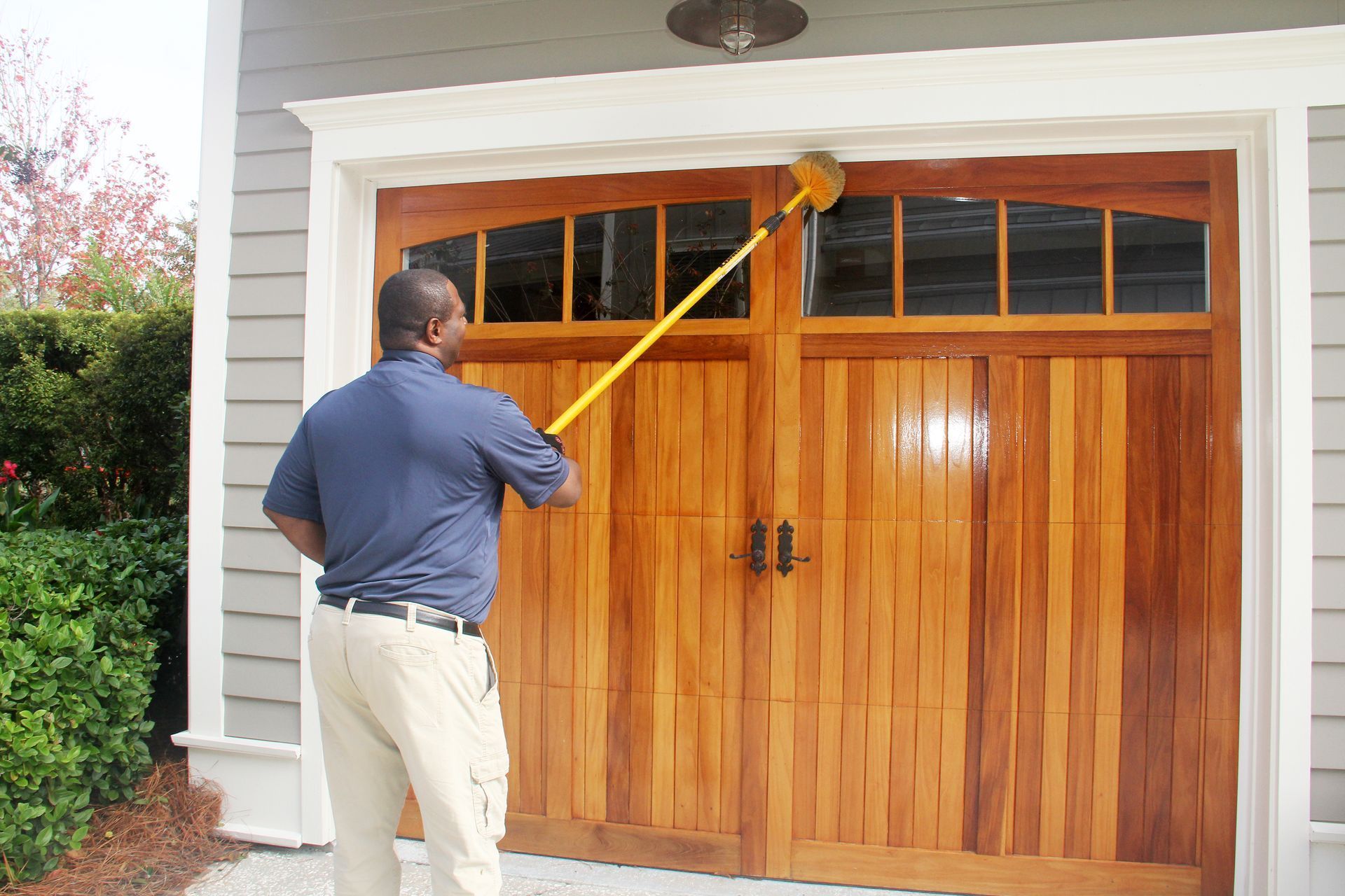 A person using a yellow pole tool to clean or seal the top edge of a wooden garage door.