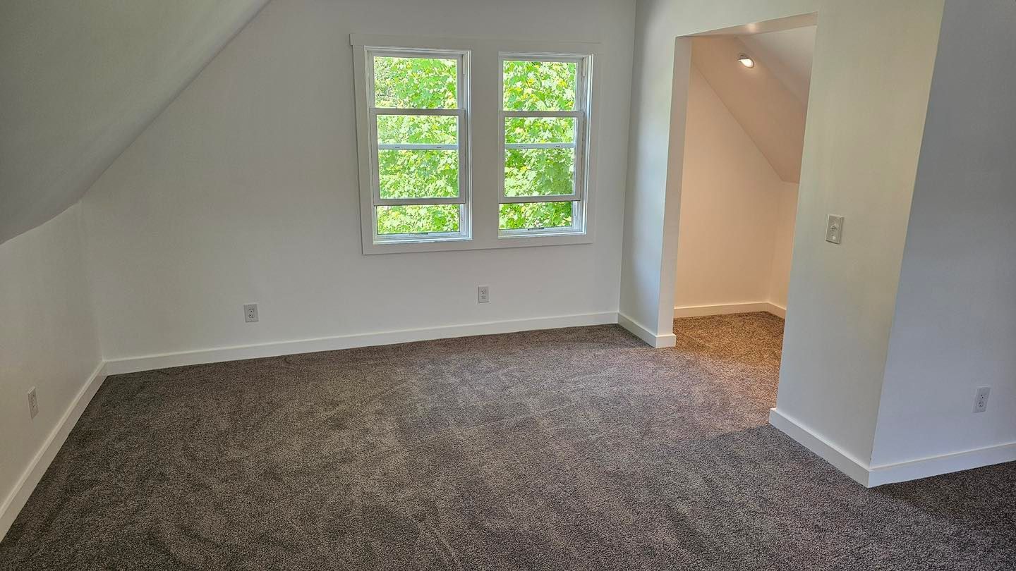 Empty room with white walls, window, and brown carpet.