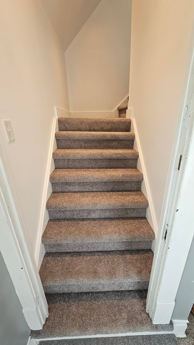 Staircase with gray carpet leading upwards between white walls, a door frame visible.