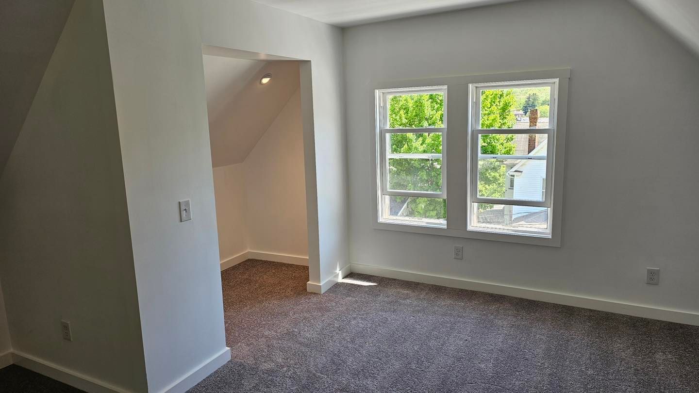 Bedroom with gray carpet, white walls, two-pane window, and closet.