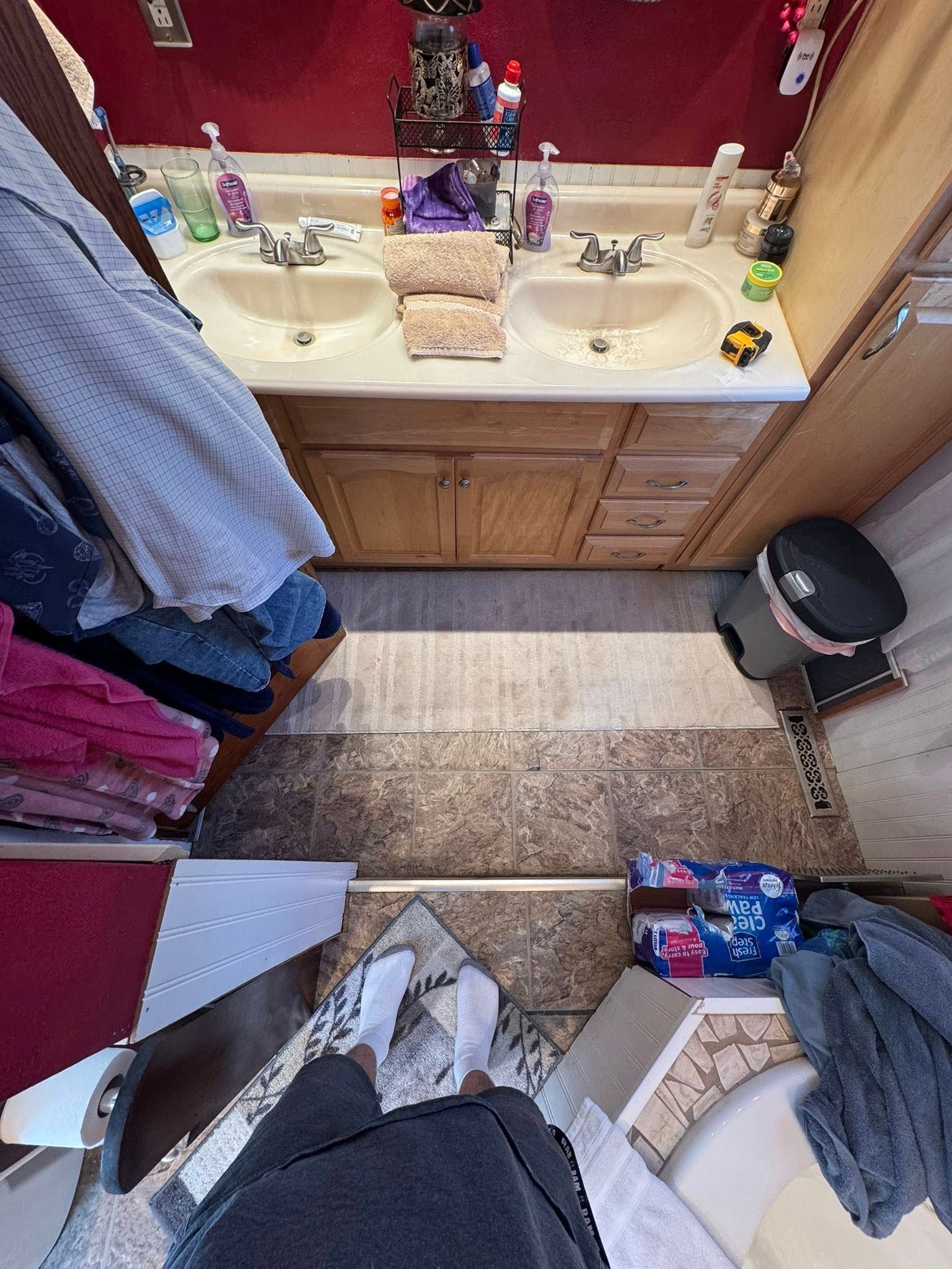 Bathroom with double sinks, towels, and clothing. A person stands near the toilet.