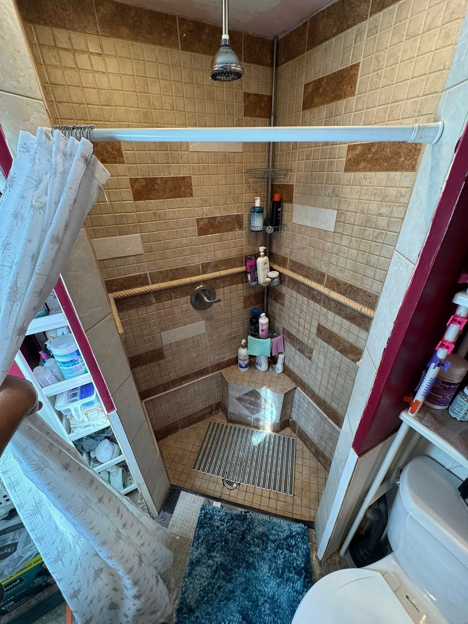 Small, angled shower with patterned tile walls and a shower curtain.