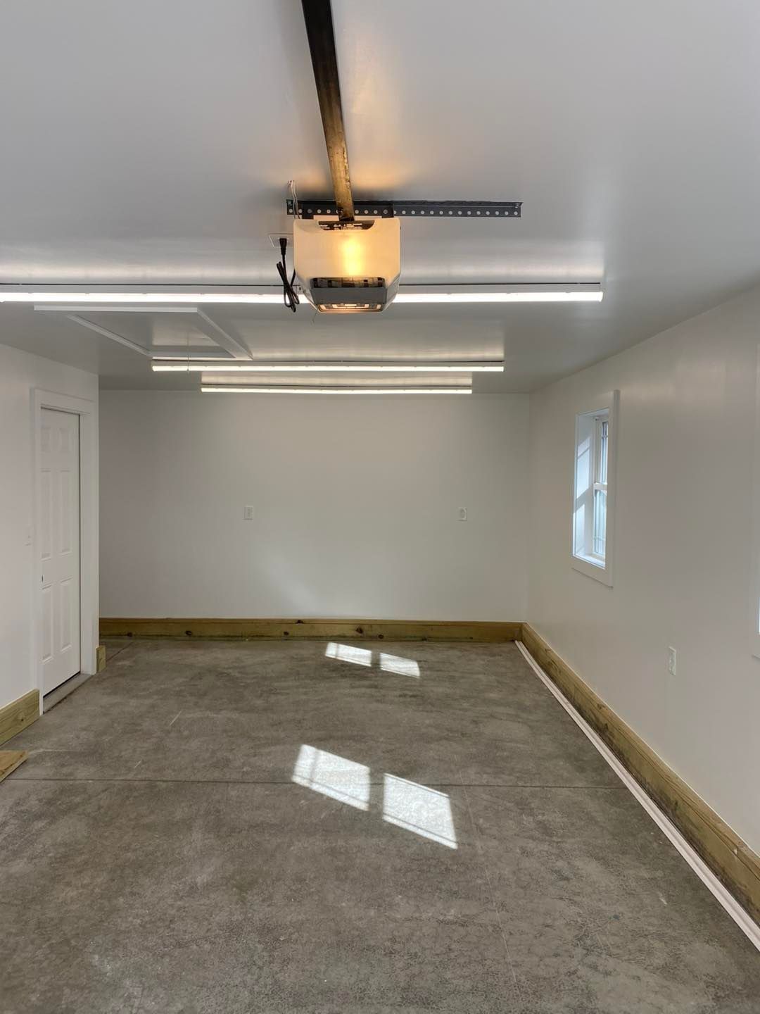 Empty, white garage with concrete floor and overhead lights.