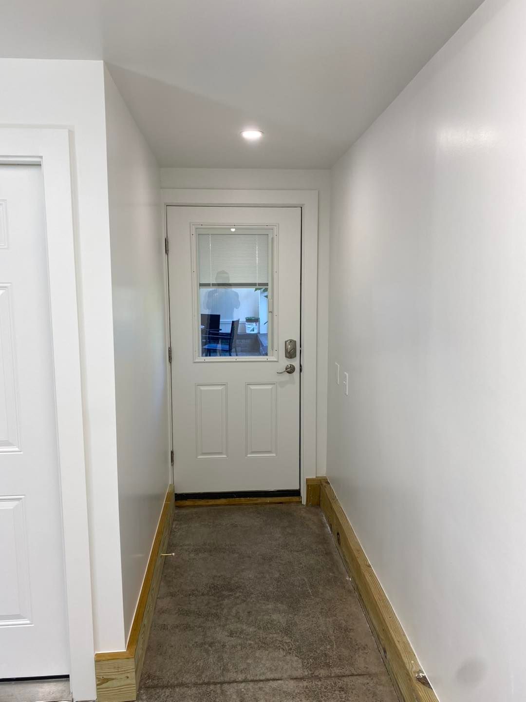 A narrow hallway with a door at the end; white walls and a concrete floor.