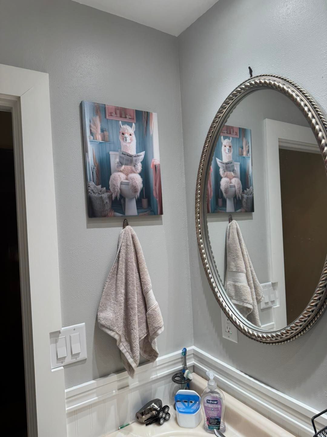 Llama art above a towel in a bathroom with a mirror reflecting the art.