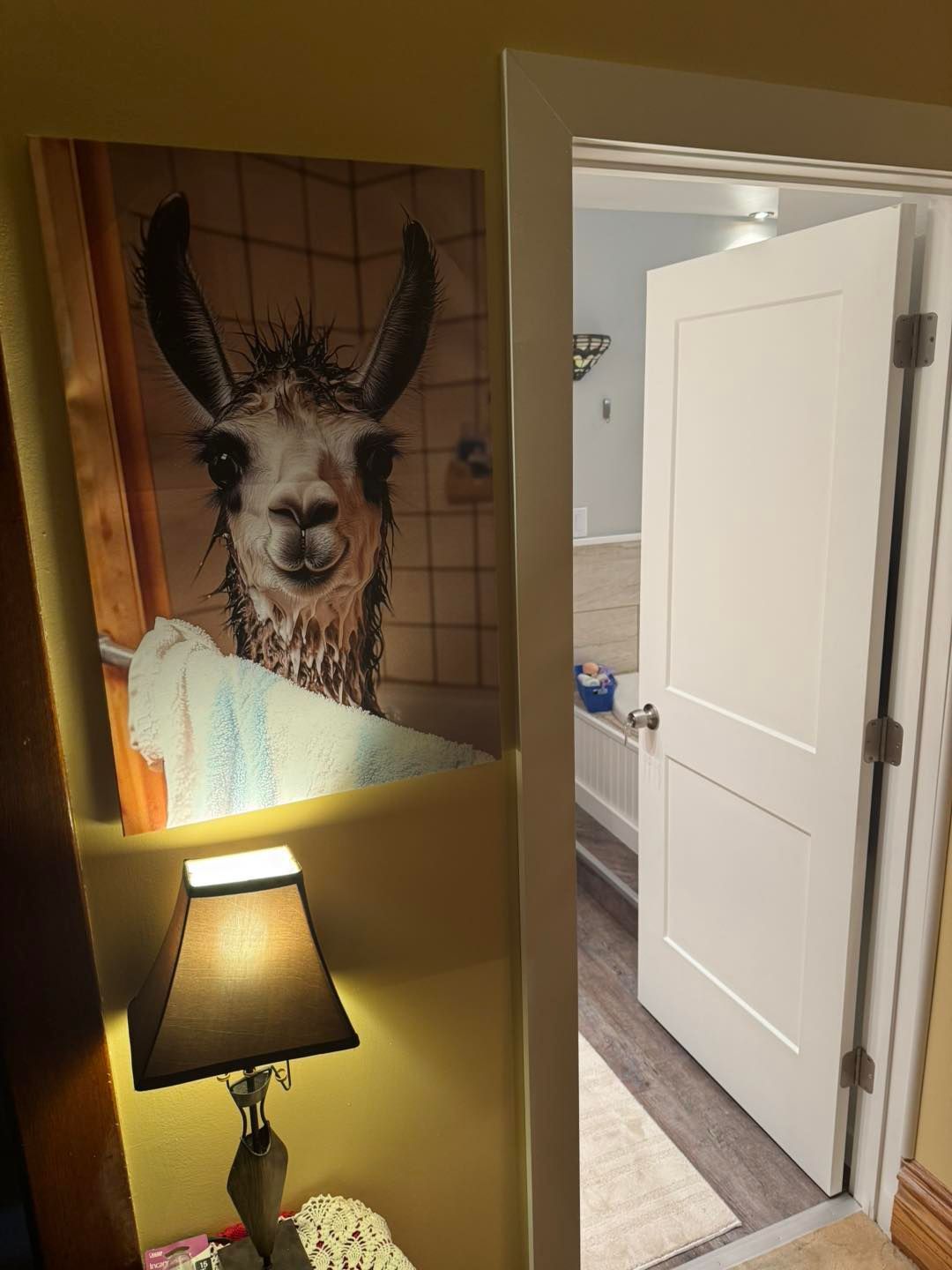 Llama portrait in a bathtub over a lamp, adjacent to an open bathroom door.
