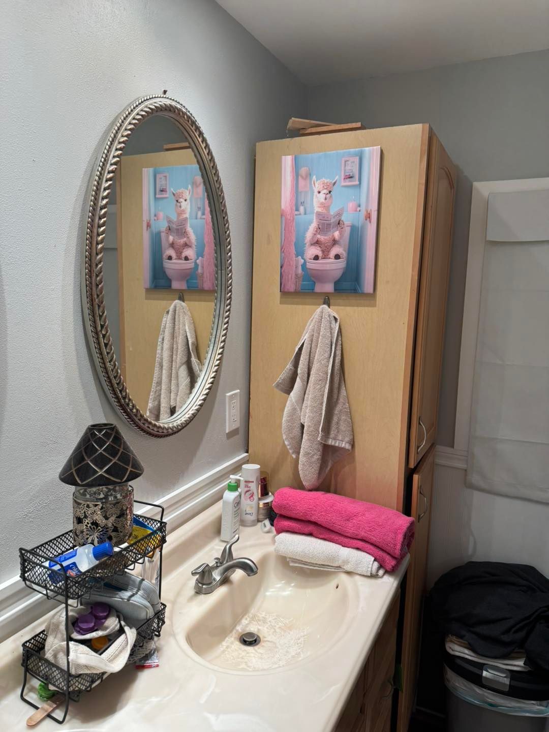 Bathroom with sink, mirror, and cabinet. Painting of an animal on the cabinet. Towels and toiletries present.