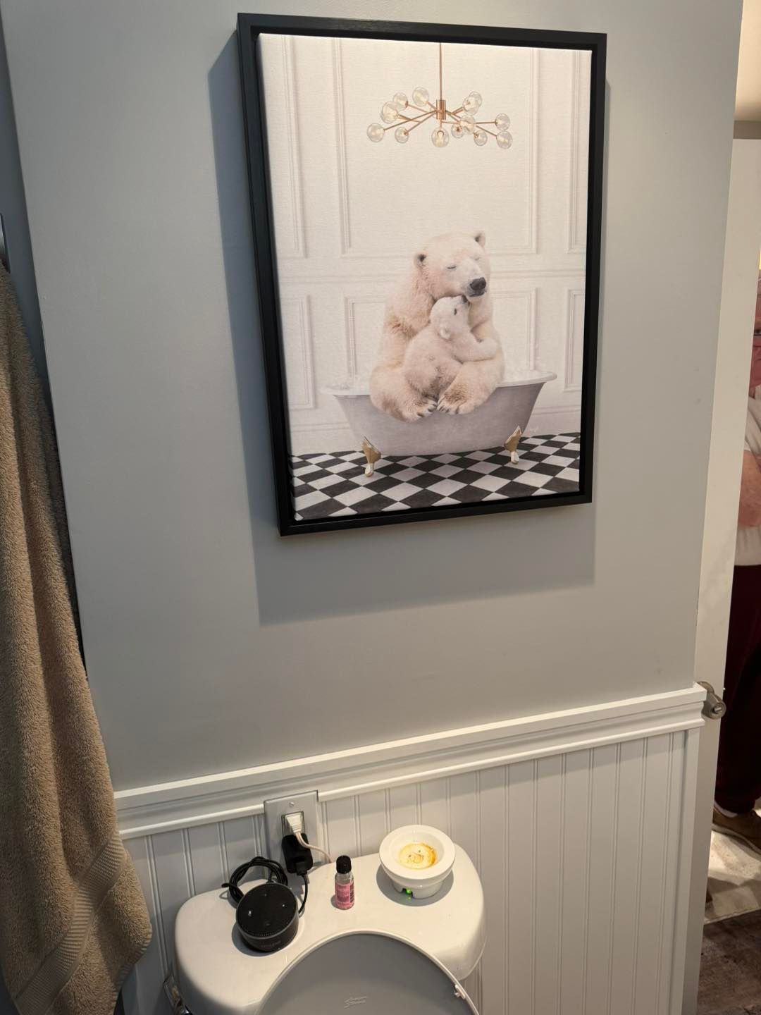 Framed art of polar bears in a bathtub, over a toilet in a bathroom with gray walls and wainscoting.