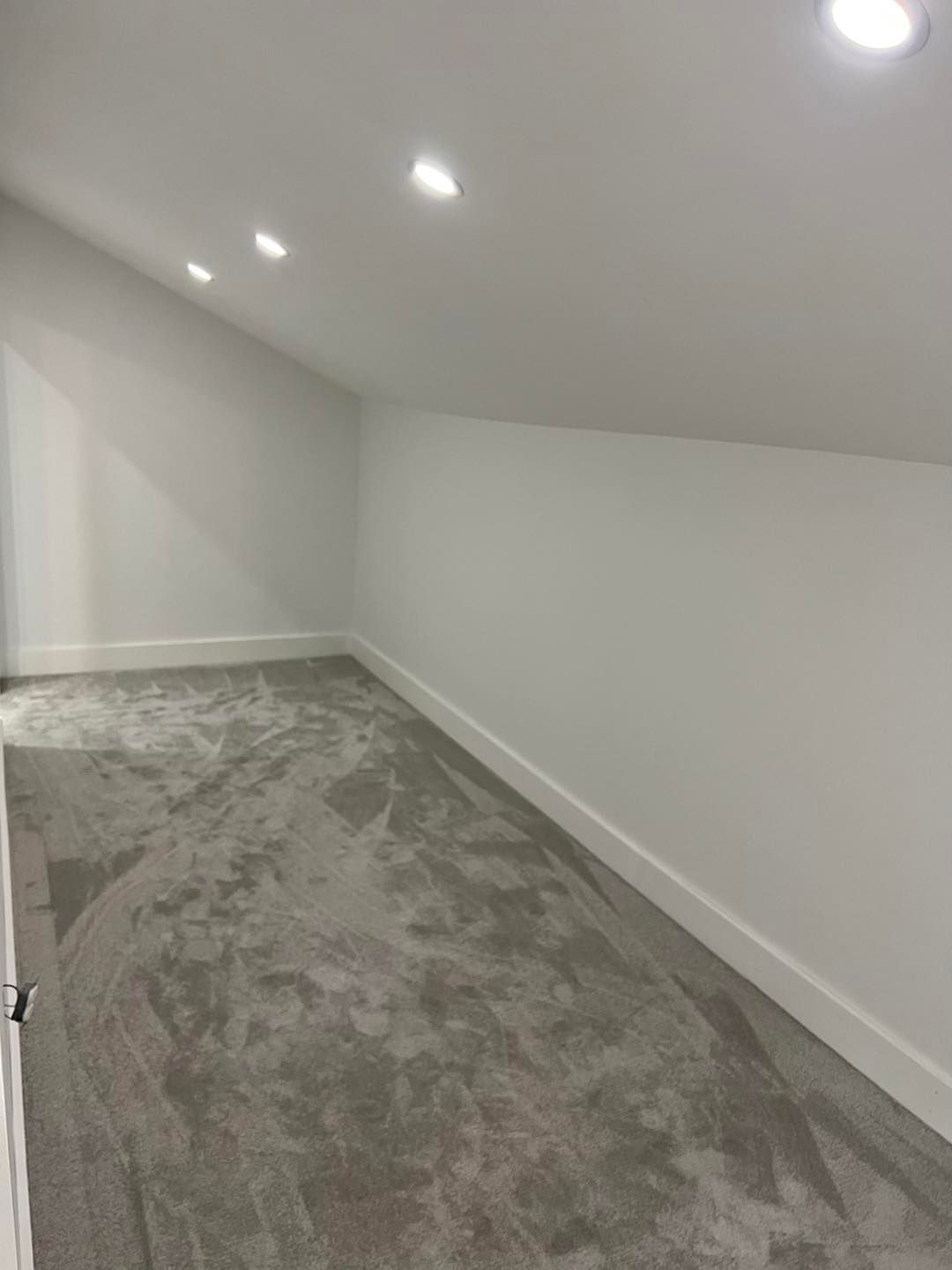 Small room with sloped ceiling, carpeted floor, white walls, and recessed lights.