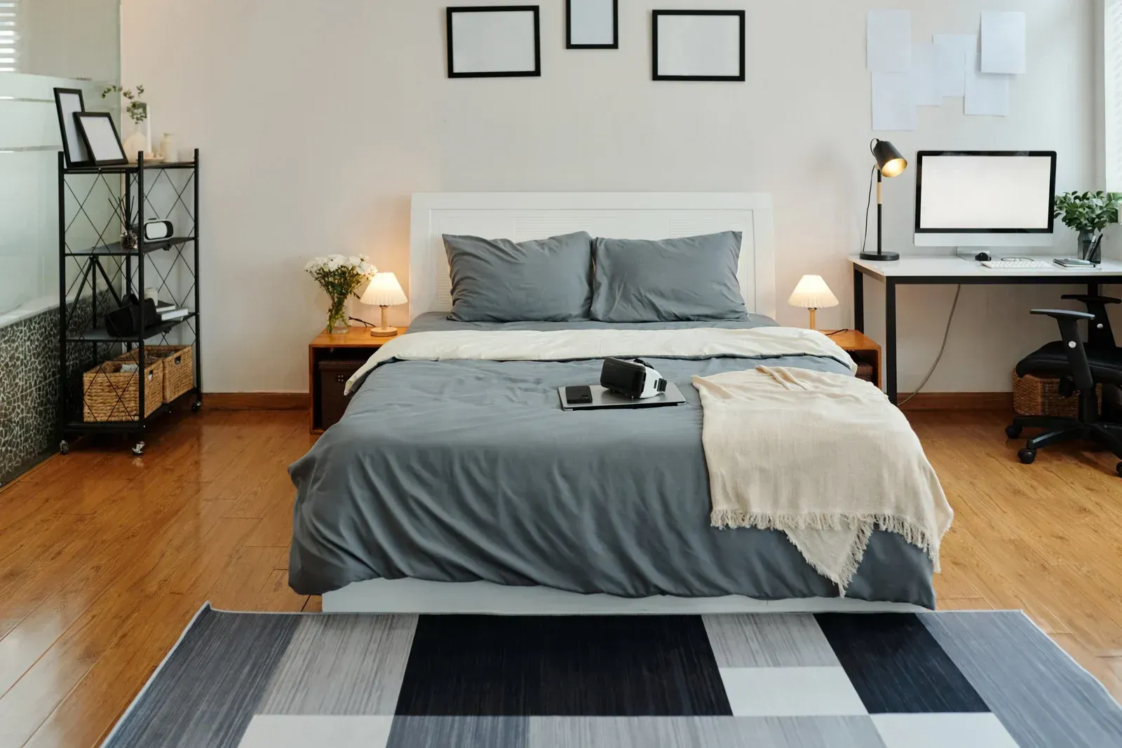 Bedroom with bed, desk, shelving unit, and decorative elements. Features wood flooring and a geometric rug.