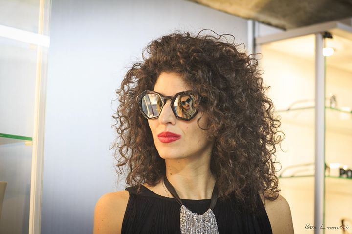 Una donna con i capelli ricci indossa occhiali da sole e una collana.