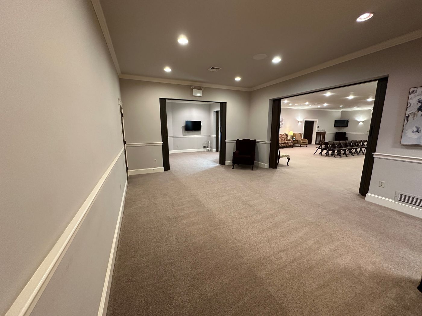 A long hallway leading to a large room with a table and chairs.