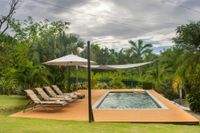 Poolside lounge with two chairs, umbrella, and a rectangular pool in a lush tropical garden