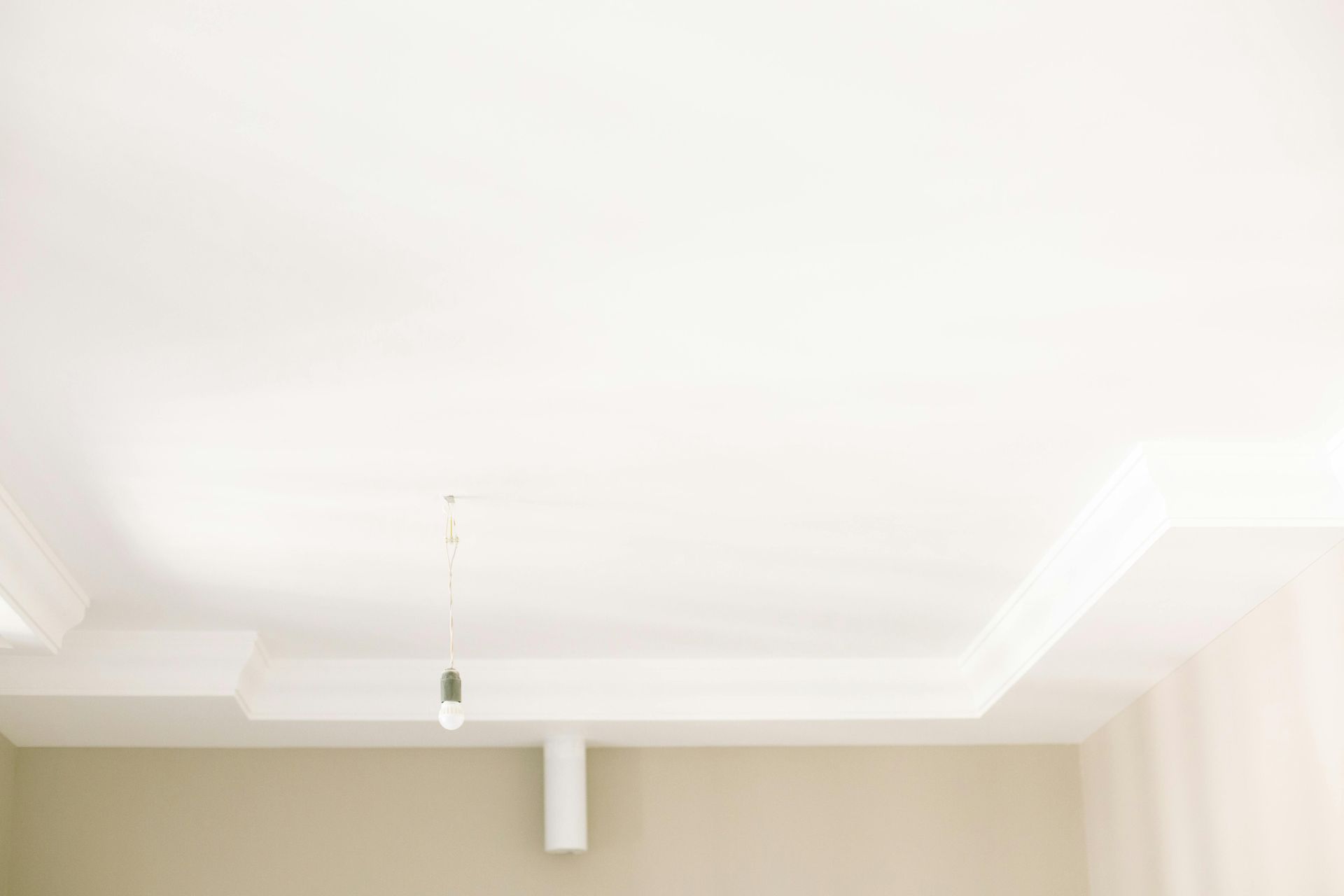 White ceiling with decorative crown molding and a single hanging light fixture in a beige room.