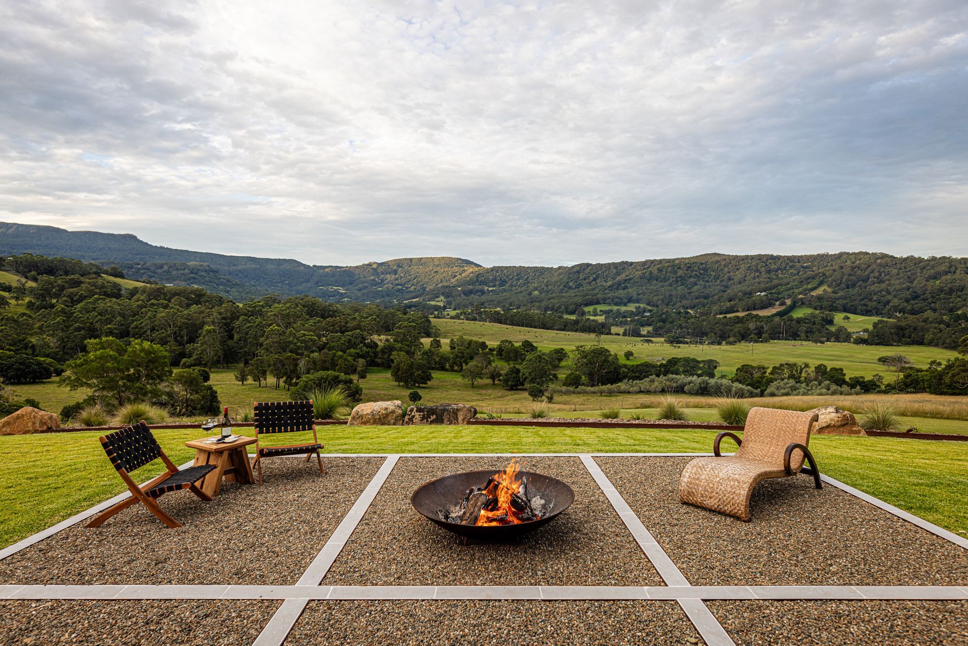 Fire pit seating area overlooking a green valley and hills under a cloudy sky — Burmah Constructions In Kangaroo Valley, NSW