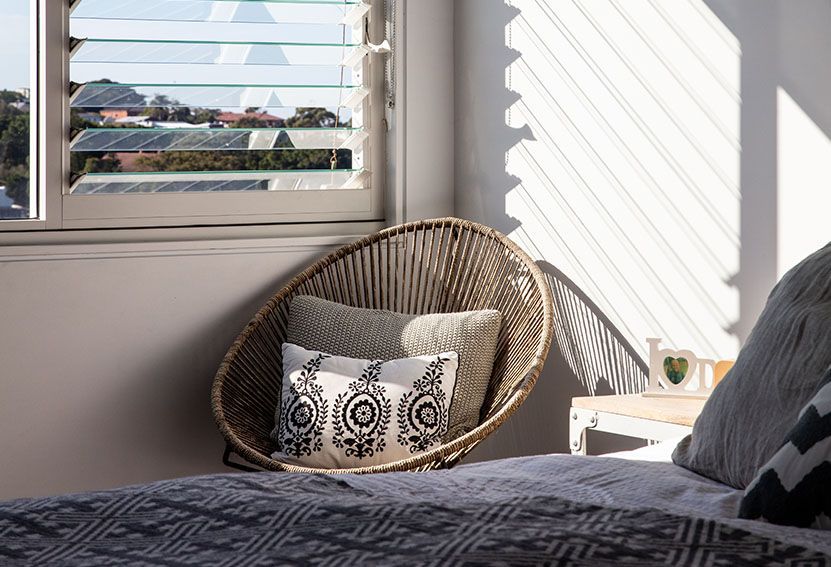 Cozy Bedroom Corner With a Wicker Chair, Pillows, and a Window Overlooking a Cityscape — Burmah Constructions In Kangaroo Valley, NSW