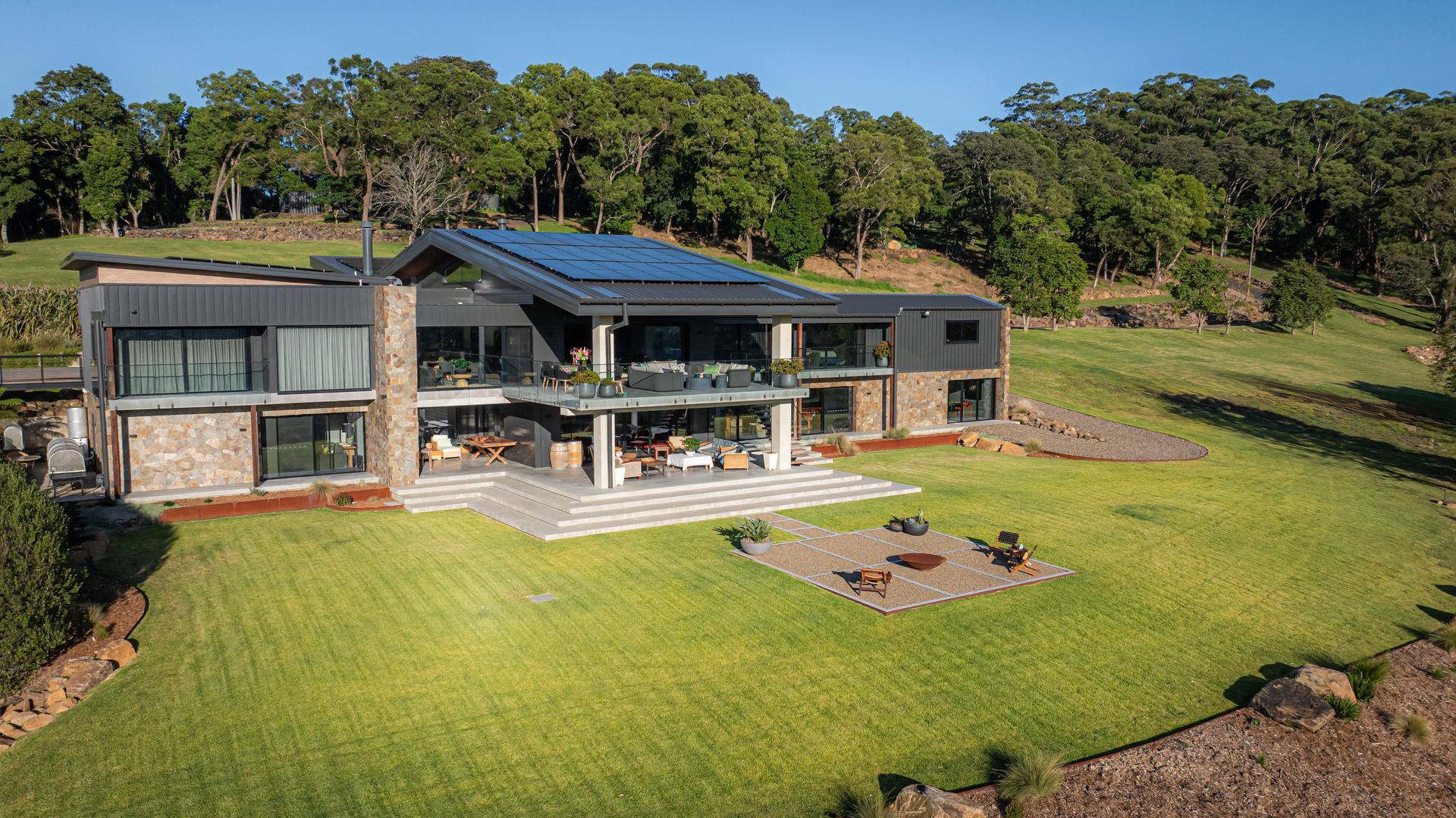 Modern house with a large lawn, solar panels, and hillside trees in the background — Burmah Constructions In Kangaroo Valley, NSW
