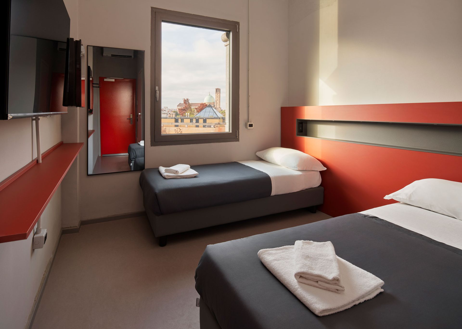 Due letti singoli in una camera con finestra e vista. Dettagli rossi e grigi.