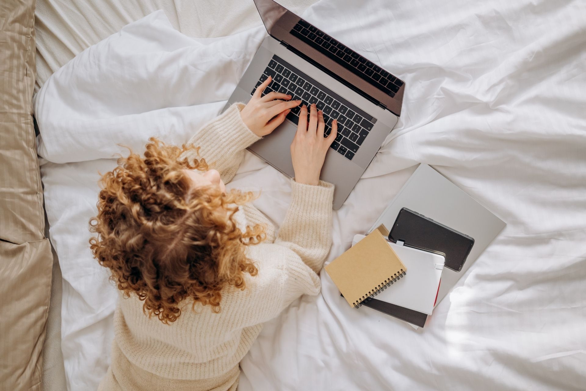 Una donna è sdraiata su un letto e usa un computer portatile.