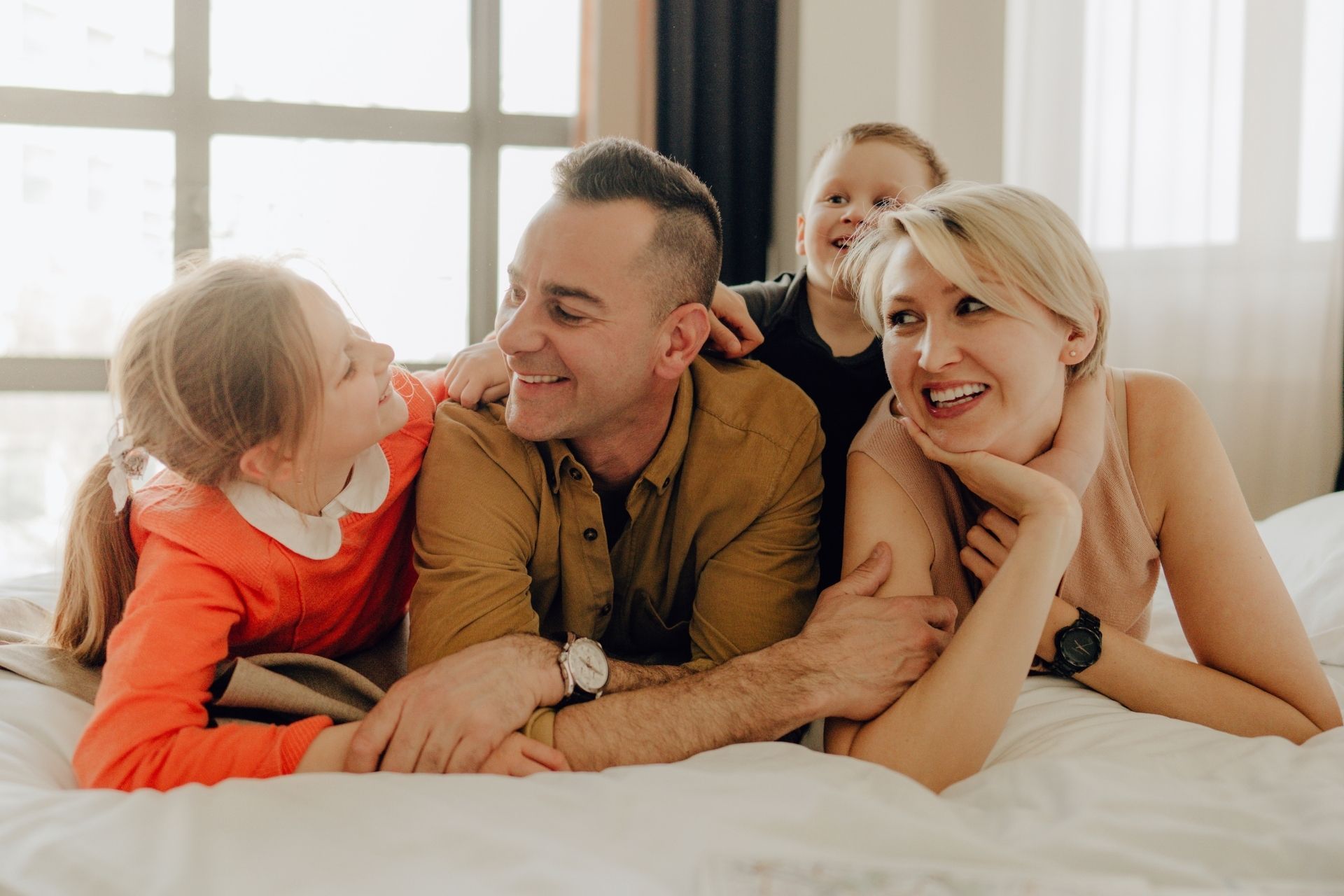 Una famiglia è sdraiata insieme sul letto e sorride.