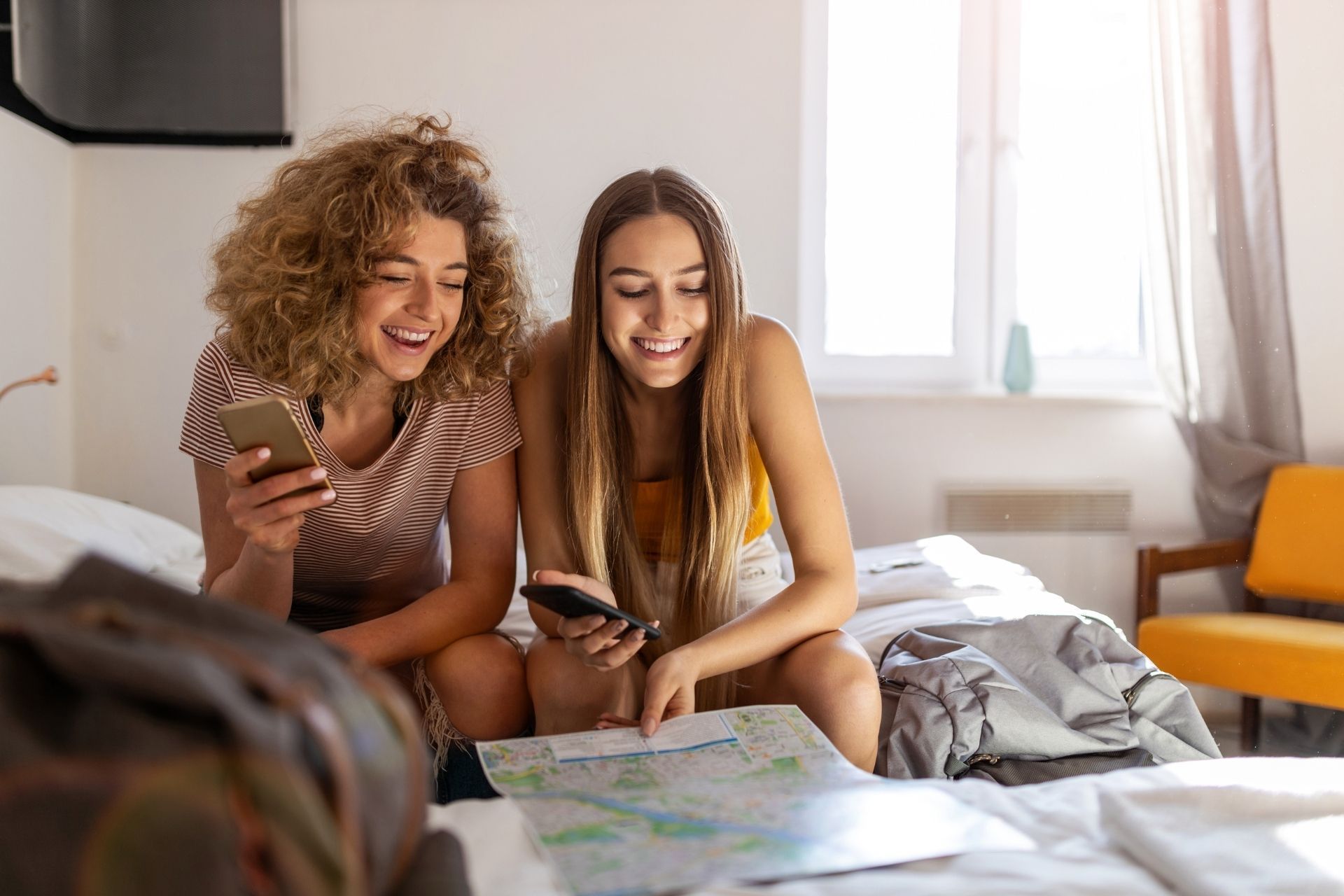 Due giovani donne sono sedute su un letto e guardano una mappa.