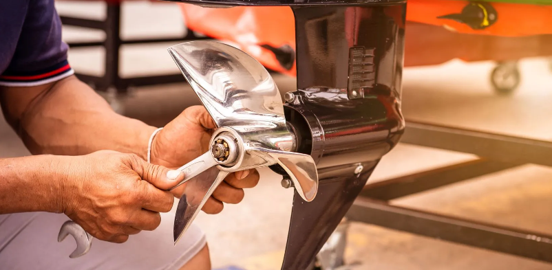 A person using a wrench to remove a propeller on a boat motor.