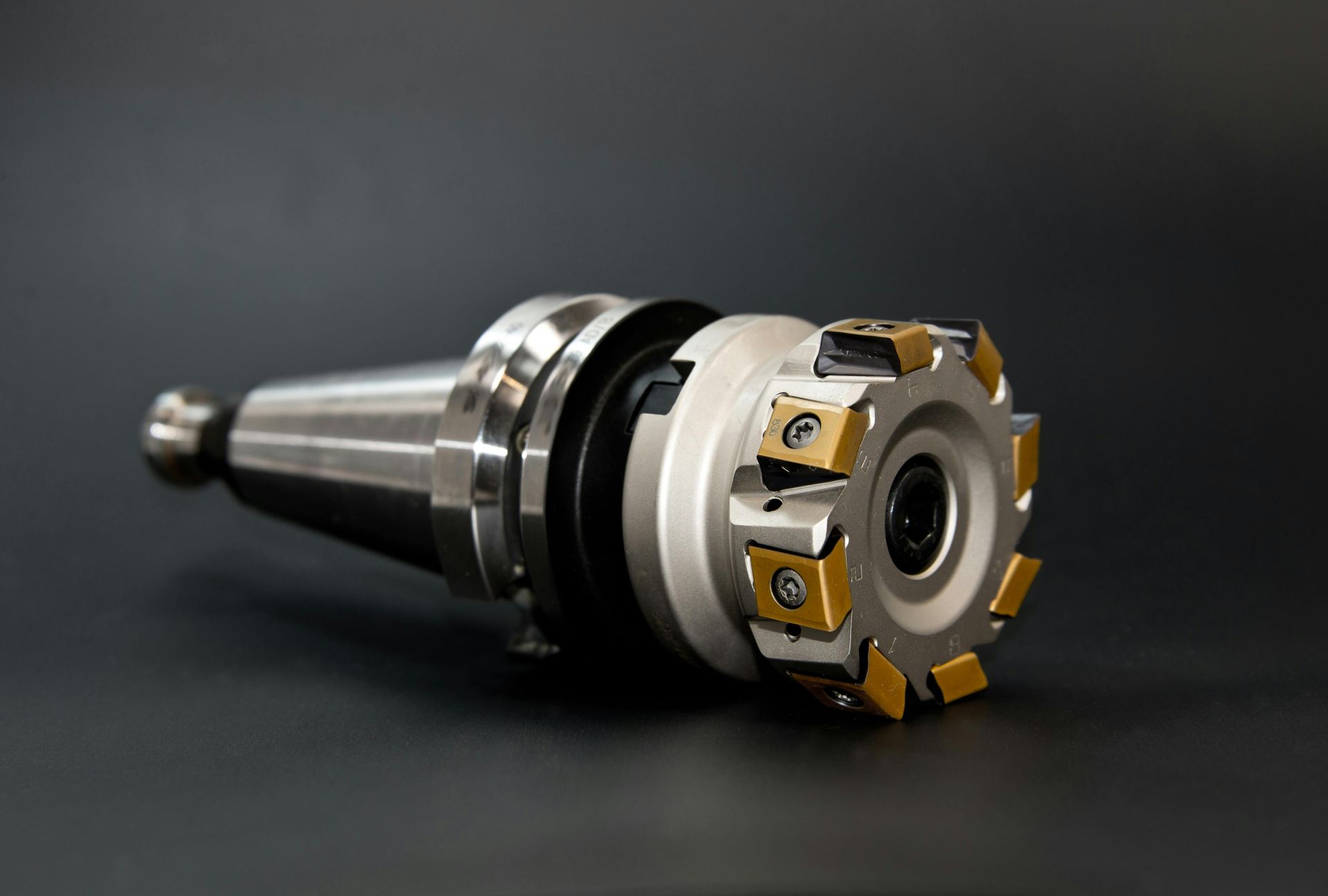 Metal milling cutter with gold inserts, angled against a dark backdrop.
