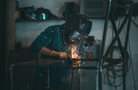 Welder wearing protective gear, working with sparks in a workshop.